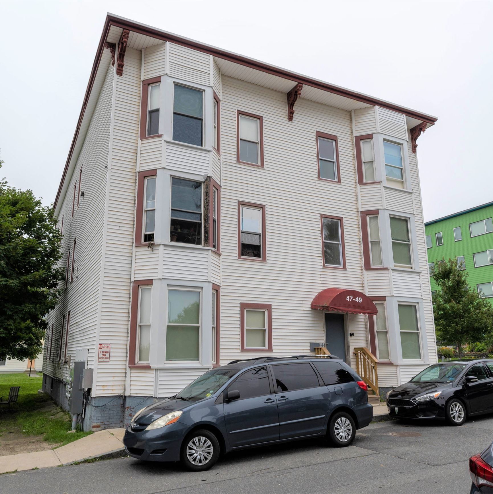 A three-story, off-white apartment building with dark red accents. 