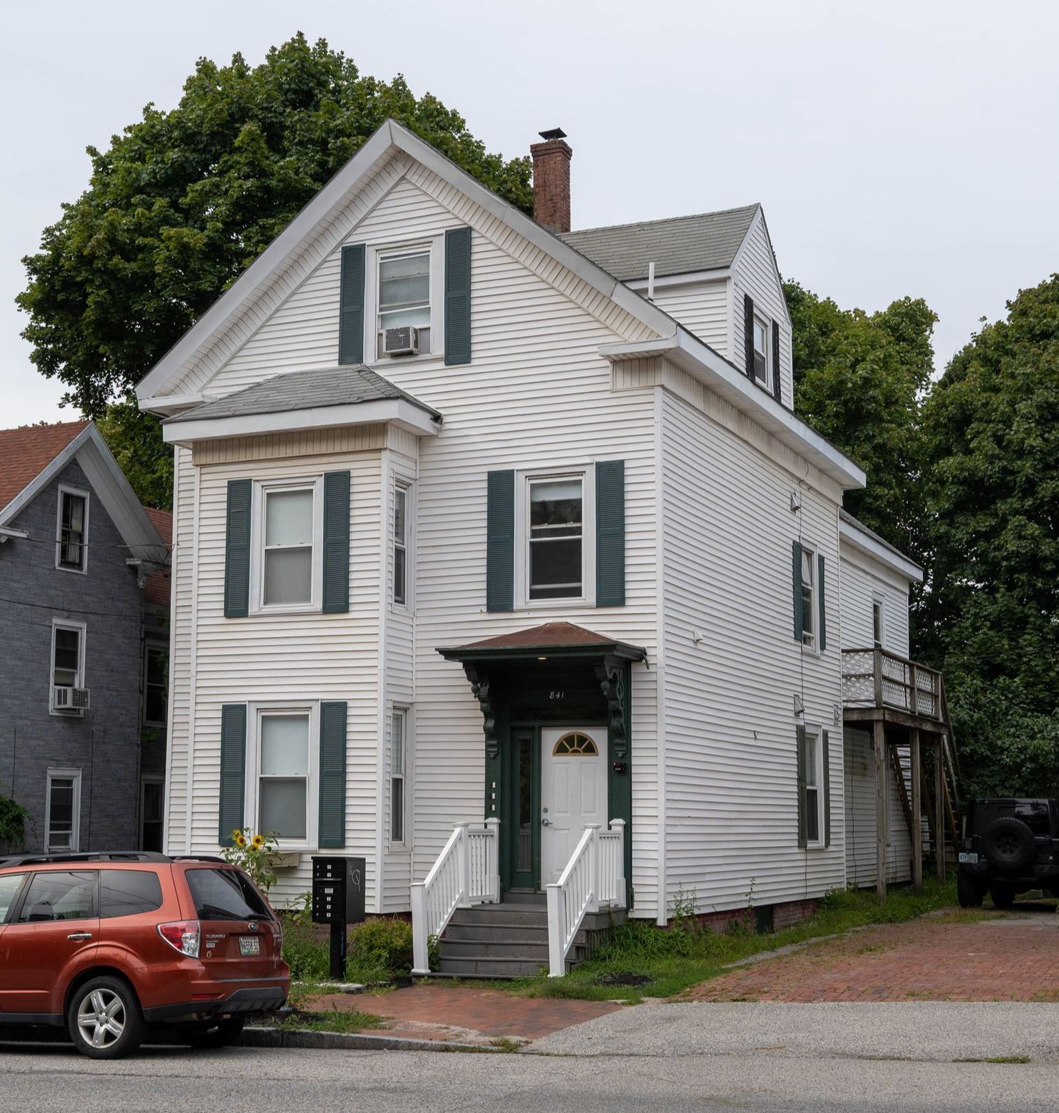 A three-story, white, classic New England Style apartment building with dark green accents.