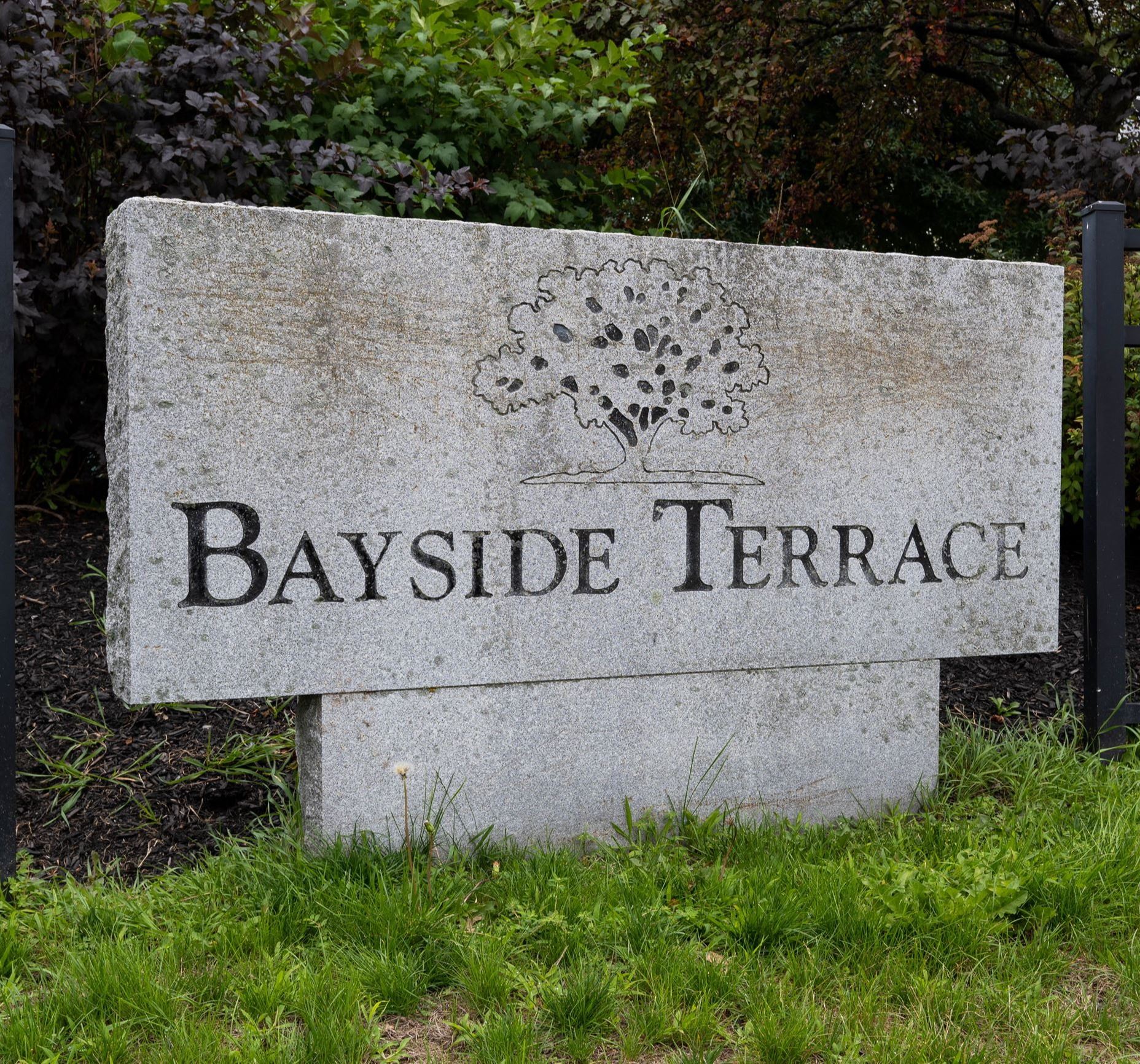 Image of a stone sign with the image of a tree that reads "Bayside Terrace"